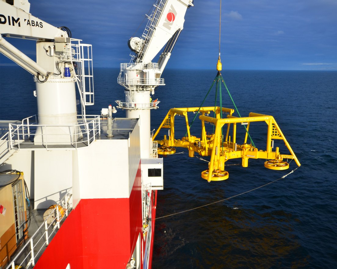 A yellow subsea structure lifted over the side of an offshore construction vessel